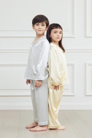 Two kids standing back-to-back in stylish Authentic Kid's Silk Pajama Sets in cream and blue.