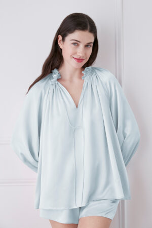 Woman in baby blue blouse and shorts set against white background, showcasing the elegance and comfort of the outfit.