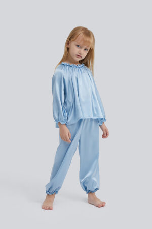 Pensive little girl in a Fairy silk loungewear set with a blue top and matching pants.