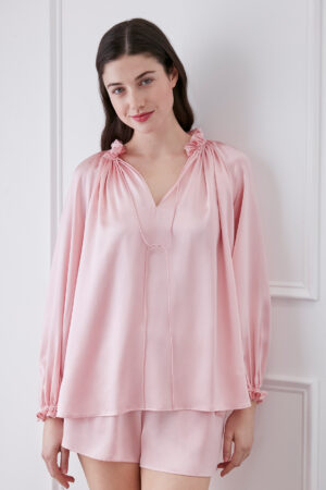 Woman in moonlight pink blouse and shorts set, smiling with ruffle trim neckline, V-neck design, and adjustable string.