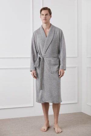 Serene elegance captured as a man stands in a flint gray wool silk knit robe by MANITO, against a crisp white interior backdrop.