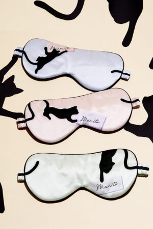 Three playful MANITO cat eye masks in different colors displayed flat on patterned background.