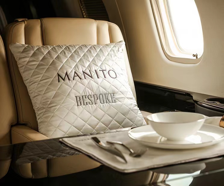 Luxury quilted silk pillow with MANITO BESPOKE monogram in private jet setting, offering personalized comfort and style