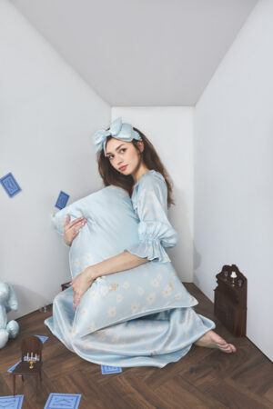 Model kneeling in a small white doll room, gently hugging a blue pillowcase from Alice Daisy Sleeping Beauty Gift Box.