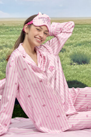 Model sitting outdoors in MANITO DISNEY Cheshire Collection Eye Mask and matching striped pajama set.