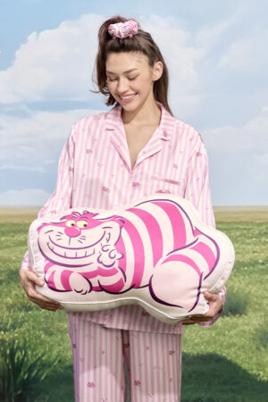 Smiling model in pink striped silk pajamas holding MANITO DISNEY Cheshire Collection Smile Face Silk Pillow.