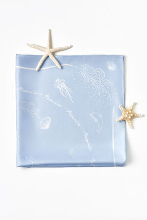 Neatly folded MANITO Ocean Blue Silk Scarf with jellyfish and dolphin line drawings on a clear blue silk background.
