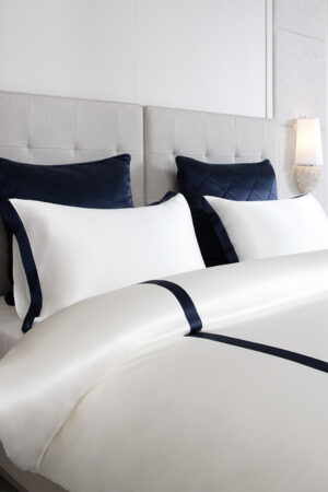 Close-up of a MANITO white silk duvet cover with navy French trim.