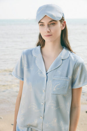 Model wearing MANITO Ocean Blue Silk Eye Mask and matching pajama shirt on the beach.